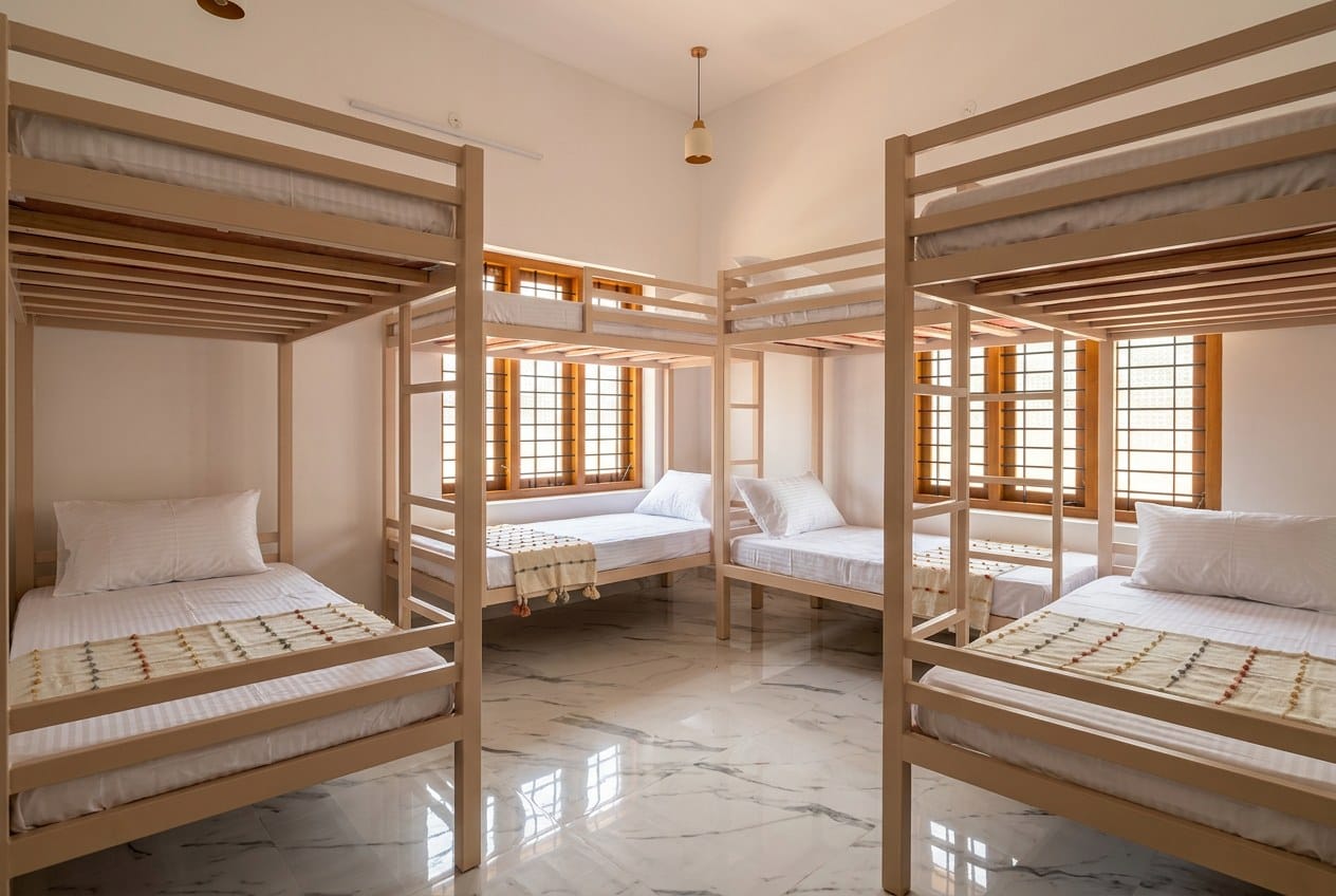 The Bunk Dorm at ZENWAYS — three pale timber bunk beds, marble floor and tall shuttered windows with warm daylight